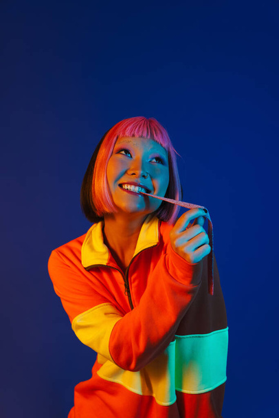 Asian girl with pink hair making fun while eating chewing marmalade isolated over blue background - 写真・画像