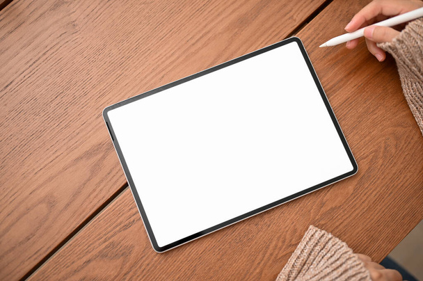 Draufsicht, Eine Frau mit Stift zeichnet auf einem digitalen Tablet-Touchpad. Tablet-Attrappe mit weißem Bildschirm steht auf hölzerner Tischplatte. - Foto, Bild