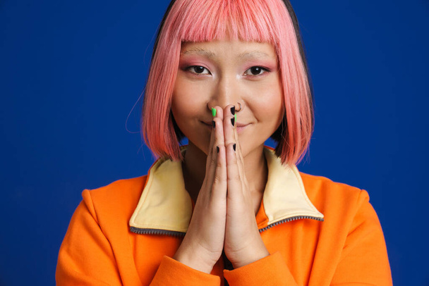 Asian girl with pink hair posing and holding palms together isolated over blue background - Foto, afbeelding
