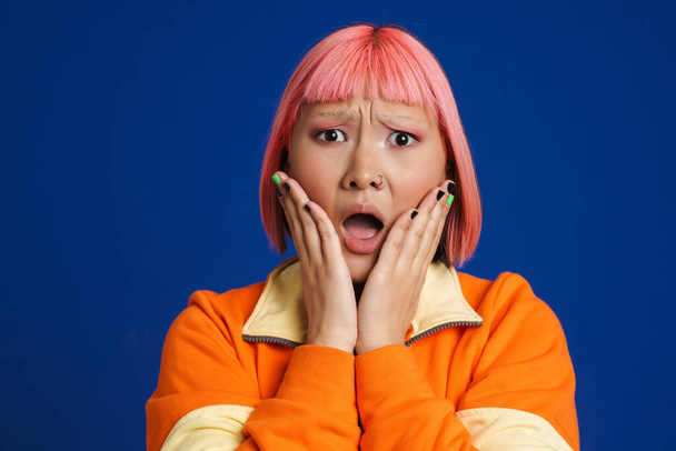 Asian girl with pink hair and piercing expressing surprise at camera isolated over blue background - Foto, Bild