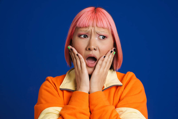 Asian girl with pink hair and piercing expressing surprise at camera isolated over blue background - Valokuva, kuva