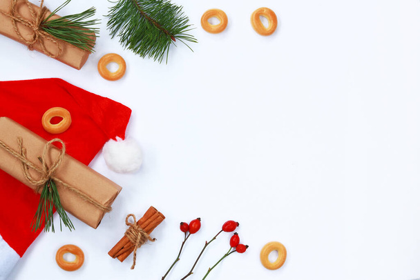 Christmas composition. Christmas gift, red New Year's cap, fir branches, bagels and cinnamon in tubules on a white background. Flat lay, top view, copy space. Happy New Year - Foto, imagen
