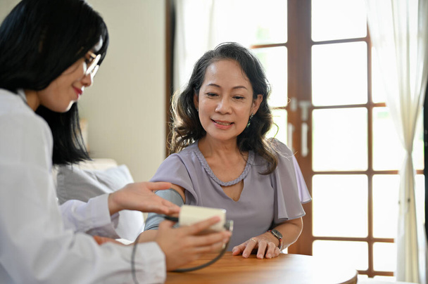 Profi fiatal ázsiai női orvos ellenőrzi a beteg vérnyomását és pulzusát vérnyomásmérővel. Egészségügyi koncepció - Fotó, kép