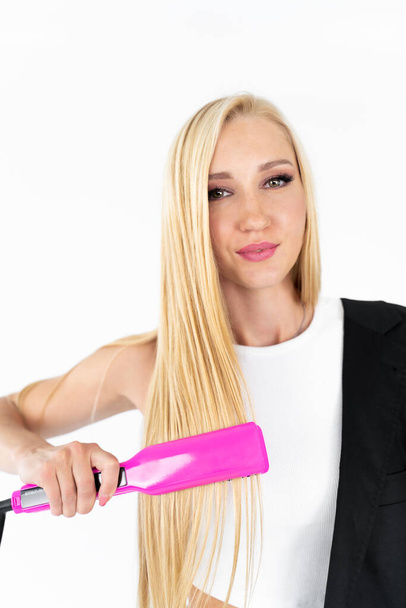 Blonde girl on a white background deletes keratin hair straightening with a pink curling iron - Photo, image