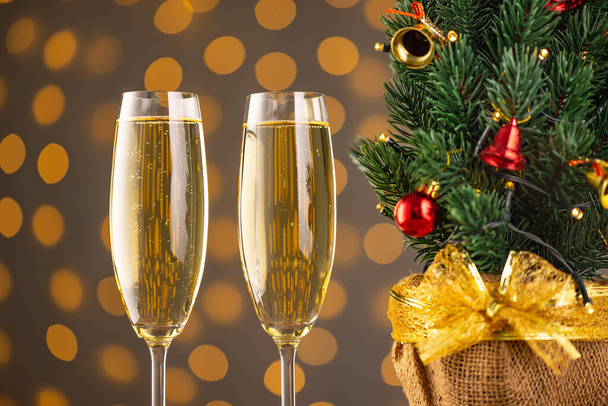 Two wine glasses with bubbly champagne and Christmas tree with decor on background of blurry sparkling lights. Happy New Year holiday greeting card, banner, header with copy space - Photo, Image
