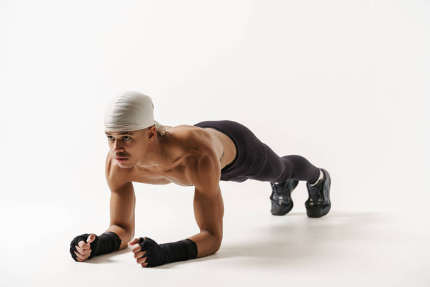 Young shirtless sportsman doing exercise while working out isolated over white background - Foto, immagini