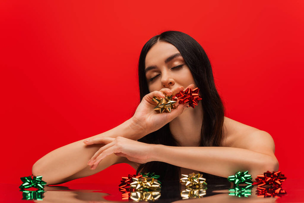 Young woman with naked shoulder holding gift bows isolated on red  - Photo, image