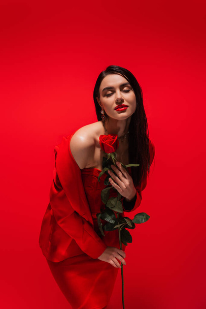 Elegant woman in jacket posing with rose flower isolated on red  - Foto, Imagem
