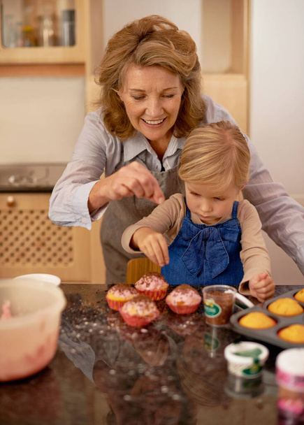 Soha nem lehet elég csokis önteted. Egy kislány, aki muffinokat dekorál a nagymamája segítségével. - Fotó, kép