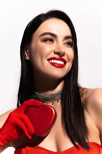 Portrait of pretty brunette woman with red lips holding heart shaped gift box isolated on white  - Fotó, kép