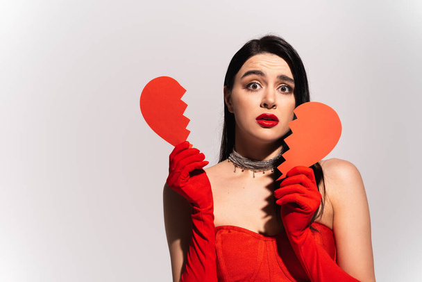 Worried woman in red gloves holding broken paper heart isolated on grey  - Foto, imagen