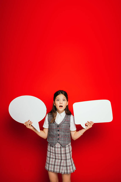 verbaasd meisje met open mond houden witte spraak bellen geïsoleerd op rood - Foto, afbeelding