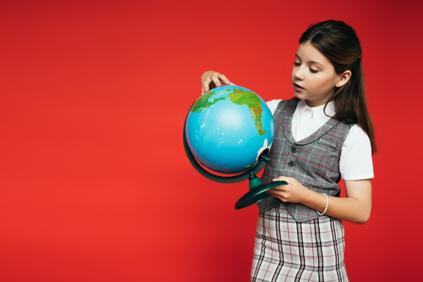 Preteen Schulmädchen in karierter Kleidung hält Globus isoliert auf rotem Banner  - Foto, Bild