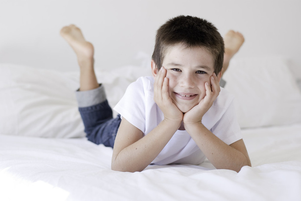 Happy young boy posing on a white bed - Zdjęcie, obraz