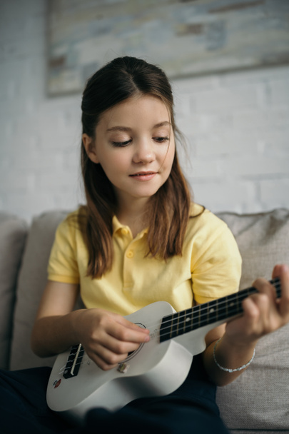 smiling girl playing small hawaiian guitar at home on blurred background - Фото, зображення