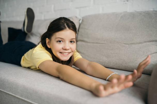 zufriedenes Mädchen schaut in die Kamera, während es sich zu Hause auf dem bequemen Sofa dehnt - Foto, Bild