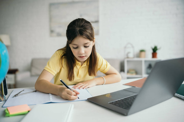 fiatal lány írás notebook, miközben tanul közelében laptop a nappaliban - Fotó, kép