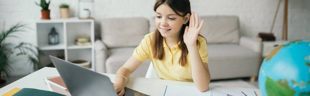 Evdeki online ders sırasında dizüstü bilgisayara bakıp el sallayan neşeli kız, afiş. - Fotoğraf, Görsel