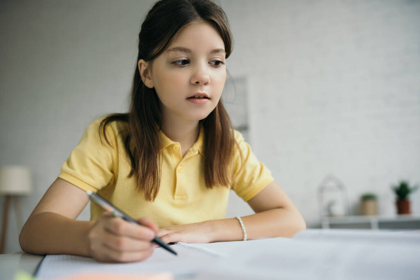 στοχαστικό κορίτσι κάθεται με στυλό, ενώ σπουδάζει στο σπίτι - Φωτογραφία, εικόνα