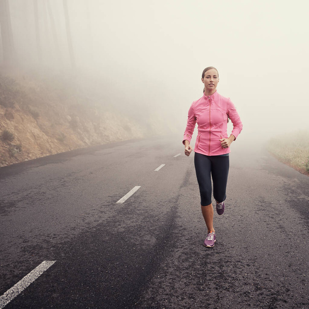 La solitude d'un jogging précoce. Une jeune femme faisant du jogging sur une route de campagne par une matinée brumeuse - Photo, image