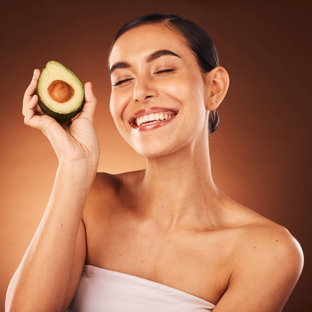 Face, skincare and avocado with a model woman in studio on a brown background to promote healthy eating. Food, health and wellness with an attractive young female inside for luxury or natural care. - Foto, afbeelding
