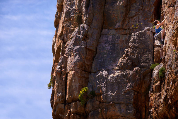 Kockázattal él... ezért szeret sziklát mászni. egy női mászó mászik egy sziklafalon - Fotó, kép