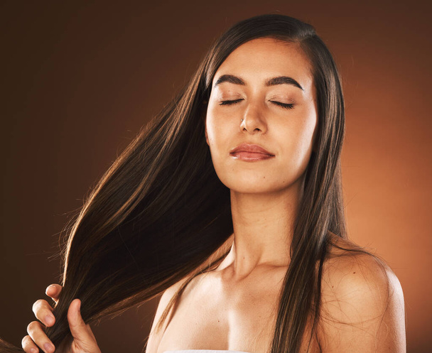Face, beauty and hair care of woman with eyes closed in studio isolated on a brown background. Skincare, makeup and cosmetics of healthy female model from Canada satisfied with salon hair treatment - 写真・画像