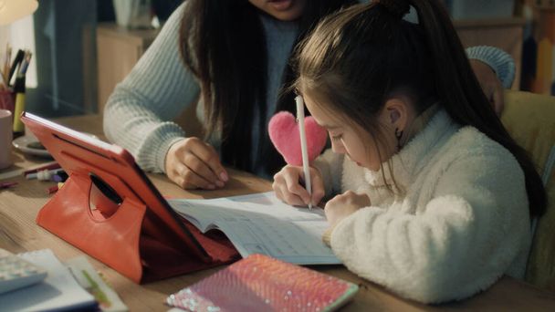 Asian family making homework, discuss new material, sitting at the table and studying together. Schoolgirl writes notes and talks with mom. Distance learning concept. Remote studying. Slow motion. - Photo, Image