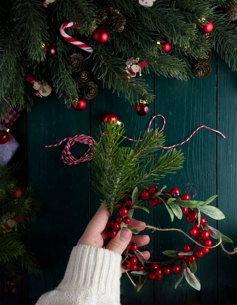 Close-up female hands decorate a Christmas wreath on a green wooden table in a Christmas decor - Photo, Image