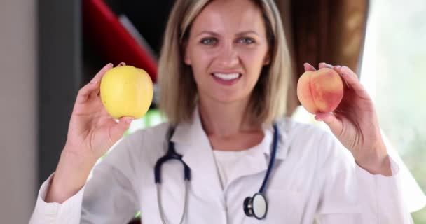 Portrét usměvavé krásné doktorky držící jablko a broskvové ovoce. Zdravotní strava a vitamíny - Záběry, video