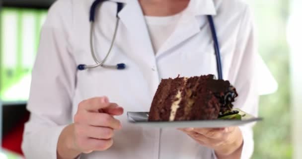 Medico mano tenendo torta al cioccolato e pollice in alto gesto di attenzione. Benefici e danni di dolci e dieta - Filmati, video