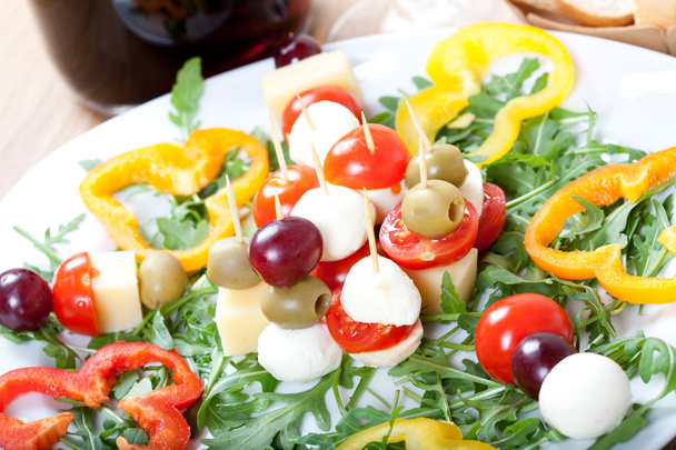 Antipasti con formaggio, mozzarella, olive e uva su piatto pieno di foglie di rucola, con vite rossa
 - Foto, immagini