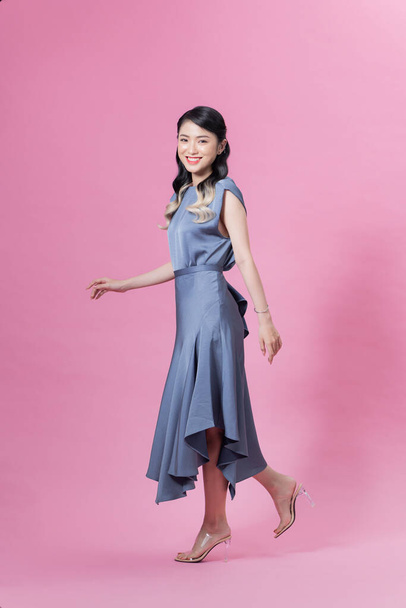 アジア系の若い女性モデルがピンクを背景に歩き笑顔で  - 写真・画像