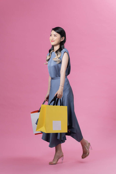 Happy beautiful woman holding many colorful shopping bags isolated on pink background - 写真・画像