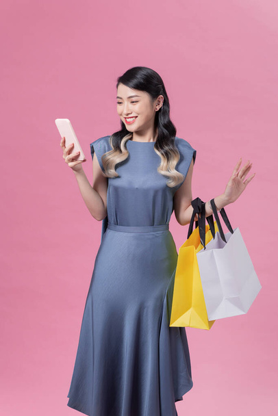 Молода щаслива азійка з барвистим пакетом магазинів користується телефоном для покупки онлайн. Здивовані великими знижками - Фото, зображення