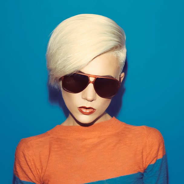 blonde with fashionable hairstyle and sunglasses on a blue backg - Фото, изображение