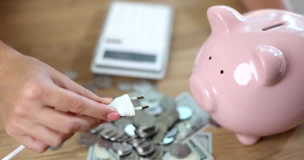 Macht vork en roze spaarvarken bankmunten en dollars met rekenmachine op tafel. Tarieven voor warmte en licht - Video