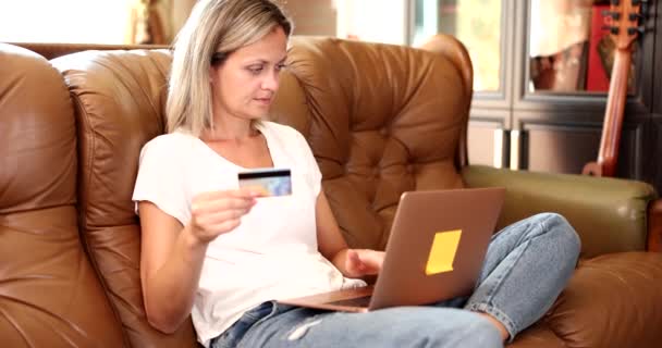 Nainen istuu sohvalla kannettavan tietokoneen ja ostoksia verkossa. Shopper syöttämällä luottokortin tiedot onnellinen nuori nainen ostoksia verkossa - Materiaali, video