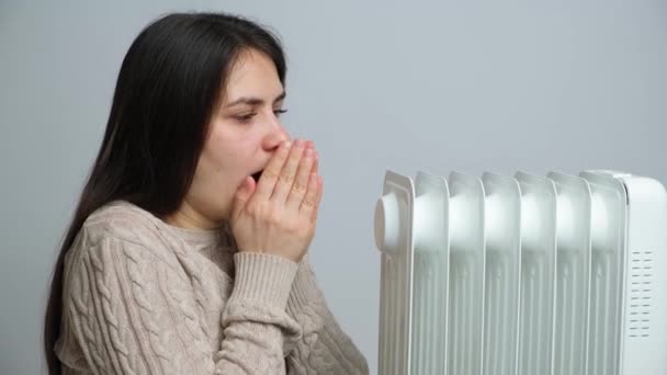 Una mujer congelada frota y calienta sus manos y abraza el calentador sobre un fondo blanco - Metraje, vídeo