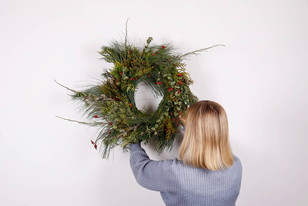 Back view of young woman hanging the holiday wreath on the wall. Traditional christmas decoration. Close up, copy space, background. - Фото, зображення
