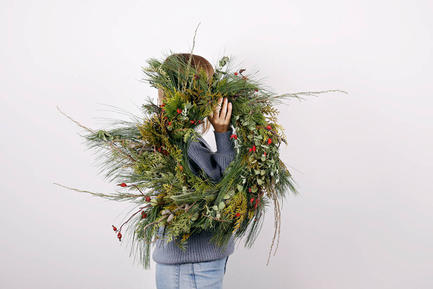 Side view of young woman holding the holiday wreath. Traditional christmas decoration. Close up, copy space, background. - Foto, imagen