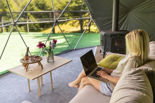 Woman working on laptop geo dome tents. Green, blue background. Cozy, camping, glamping, holiday, vacation lifestyle concept. Outdoors cabin, scenic background. - Photo, image