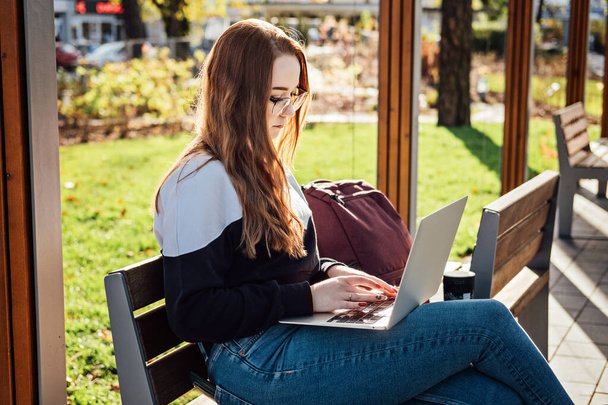 Mental health. Work-life balance, online work job or education. Redhead woman working typing on laptop outdoors. Freelancer, student girl sitting on bench in park, urban city street style. - Photo, Image