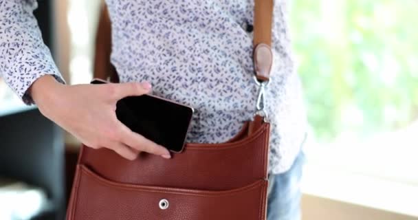 Γυναικείο χέρι βάζει μοντέρνο smartphone σε καφέ δερμάτινη τσάντα. Τσέπη τηλεφώνου σε τσάντα - Πλάνα, βίντεο