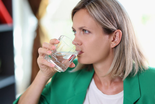 Zbliżenie nieszczęśliwej kobiety z poważną twarzą pijącej wodę niegazowaną. Odwodnienie, problemy zdrowotne i koncepcja stresu. - Zdjęcie, obraz