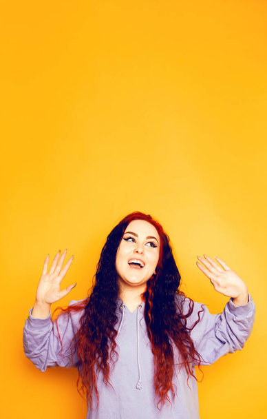A girl with frizzy and split ends on an orange background in a blue sweatshirt poses. Beautiful brunette. Smile happy  - Фото, изображение
