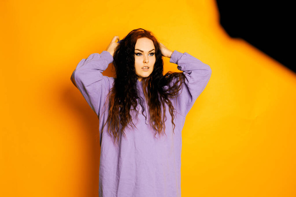 La chica en la sesión de fotos en el estudio posando sobre un fondo naranja. Modelo en sudadera púrpura - Foto, Imagen
