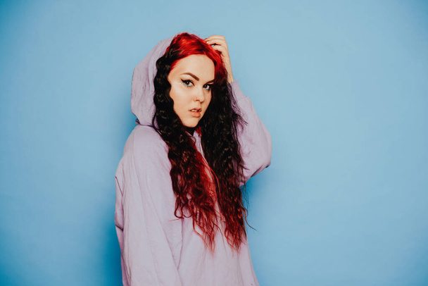 Woman in a blue sweater on a blue background posing. A beautiful brunette with long hair and and tunnels in her ears. Eyeliner and trendy makeup - Foto, Imagem