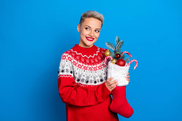 Portrait of nice woman with short hairdo hold christmas sock full of candies baubles look empty space isolated on blue color background. - Foto, immagini
