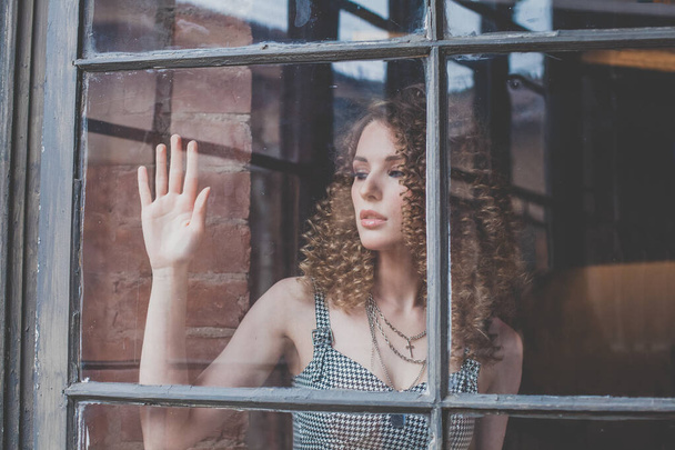 Beautiful attractive pensive woman with curly hait and touching window glass - Фото, зображення